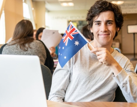 Dedicated Male College Student at the classroom looking at the camera holding an Australian flag